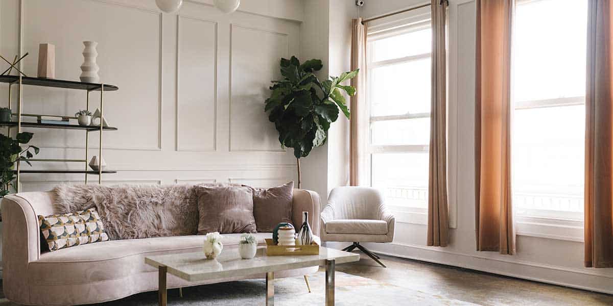 Alt Text: Bright living room featuring beige eggshell painted walls with decorative molding, a pink plush sofa, and natural window lighting.
